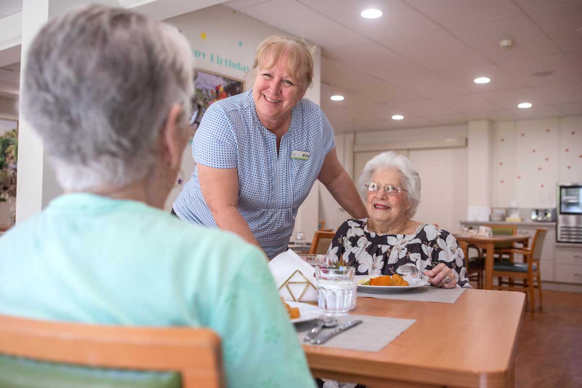 Elderly residents having dinner together with food service person smiling