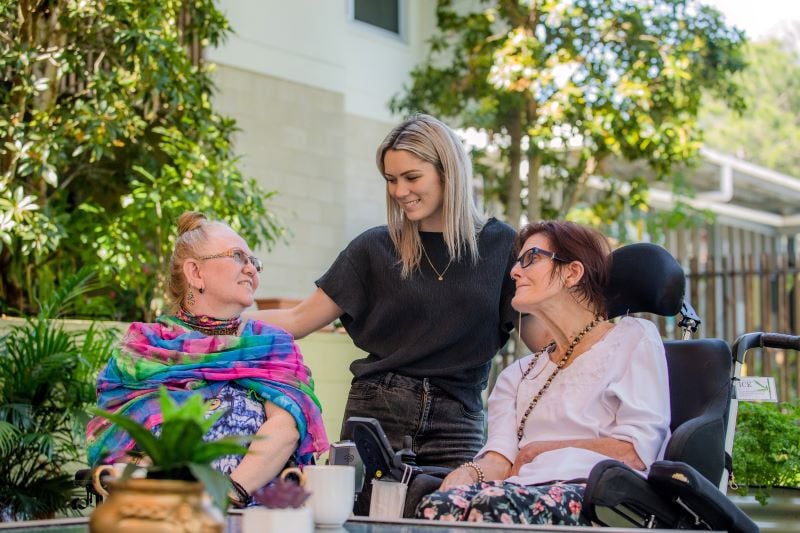 Staff member smiling with two ladies in wheelchairs
