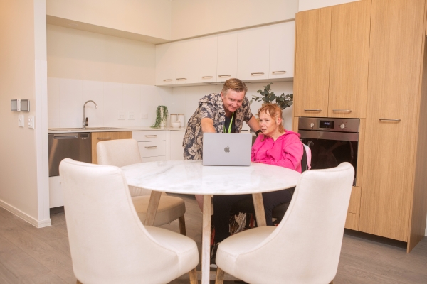 A resident and support worker looking at a laptop screen in the dining room.