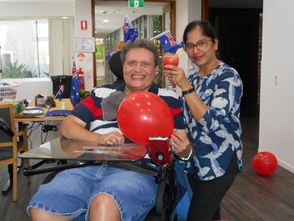 Man in wheelchair and lady smiling with balloons and flags