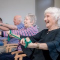 Older people smiling and exercising together in chairs with therabands