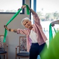 Lady exercising in group class, holding theraband over her head and leaning to the side