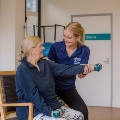 Staff helping client with dumbell as client sits in chair