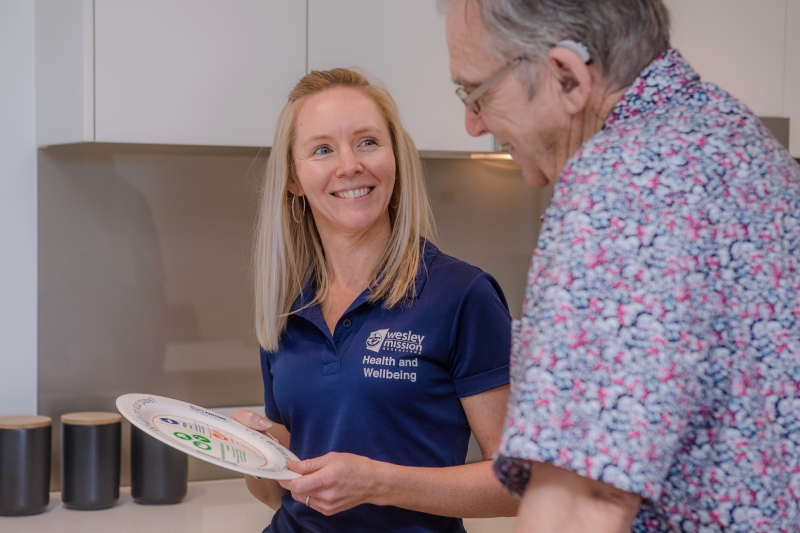 WMQ dietician holding a plate, explaining portion sizes to an elderly client