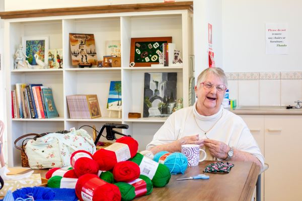 Lady smiling and knitting at table with several yarns of wool