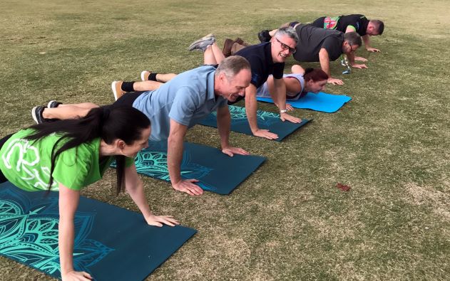 Group of people doing push ups on mats on grass