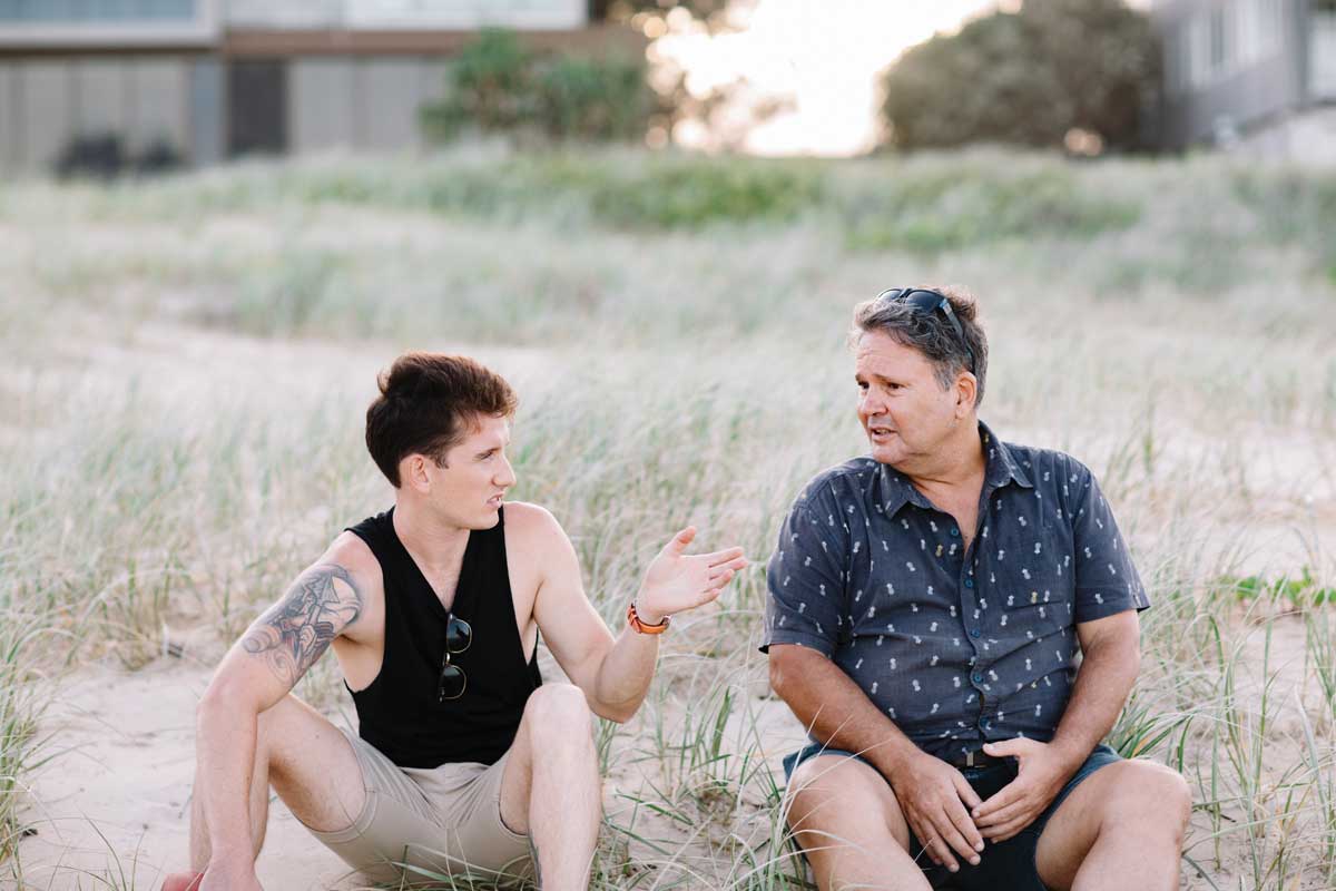 Two men sitting on the sand chatting