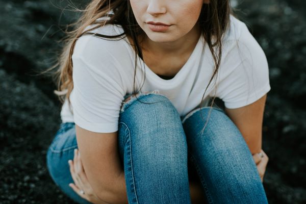 Woman sitting on ground with arms around knees