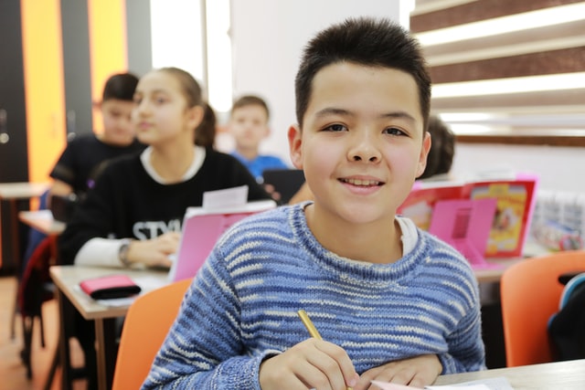 School age child smiling at camera with pencil in hand