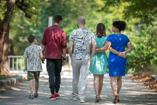 Parents and three primary school aged children walk away from camera with arms around each other