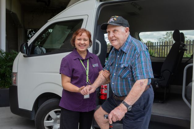 Staff member assisting resident in front of a courtesy bus