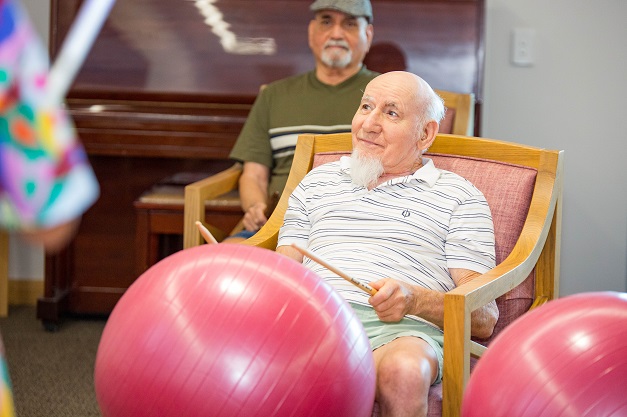 Gentleman smiling whilst holding drum sticks and participating in gentle drumming exercises