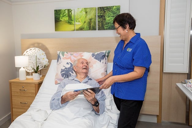 A gentleman lying in bed and being handed a book by a carer