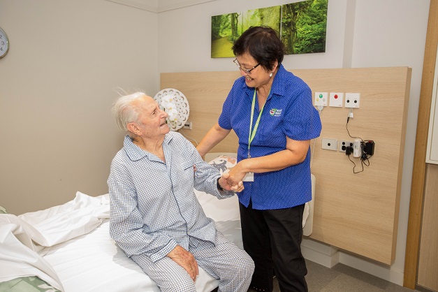 A gentlemen sitting on a bed and being helped into bed by a carer