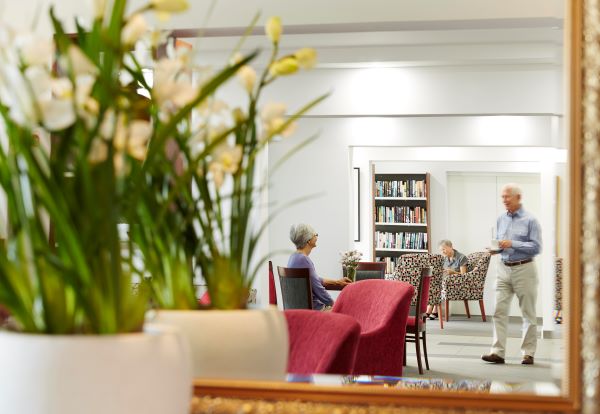 Retirees meeting in common area, seen through mirror with plant in foreground