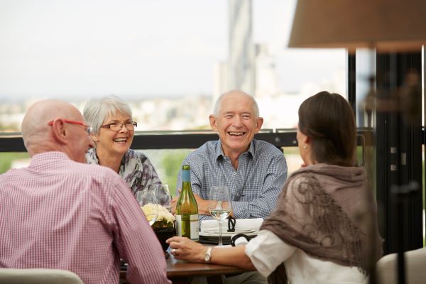 Aldersgate's strong community Group of retirees drinking on balcony at Aldersgate retirement village, with Brisbane's skyline in the background