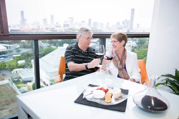 Couple enjoy drinks on balcony with views of city behind