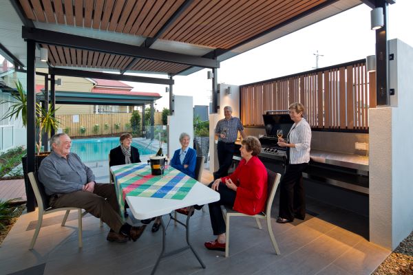 Group enjoying outdoor barbeque in undercover area by pool