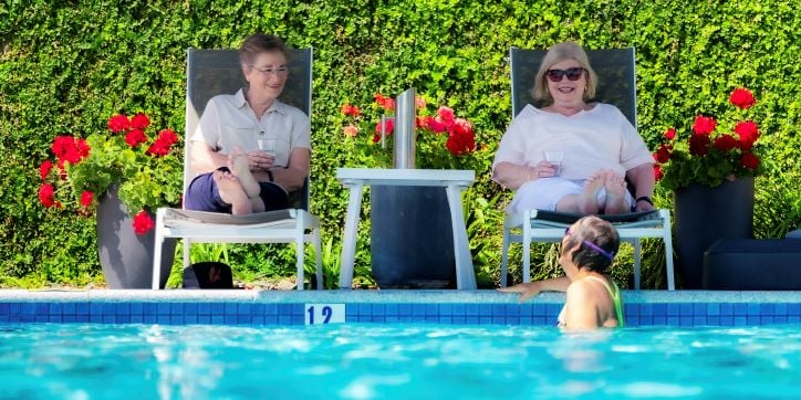 Two residents relax and chat poolside at Rosemount Sinnamon Park retirement village in Brisbane