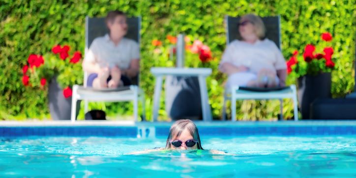Lady swimming in foreground while two ladies sit on pool chairs in the background
