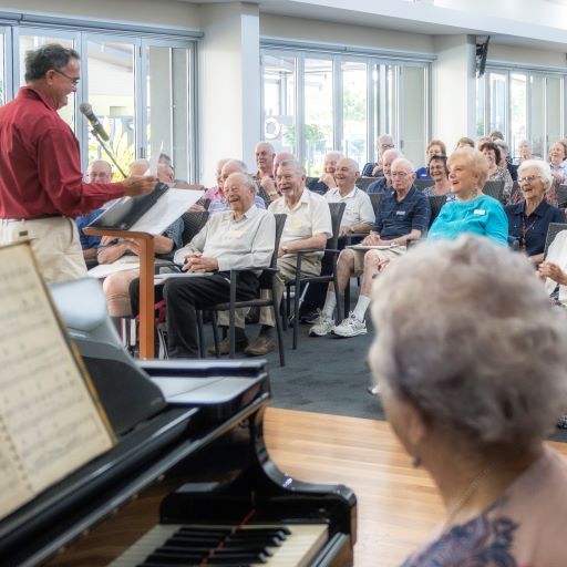 Lady at piano and man at microphone in foreground with smiling audience