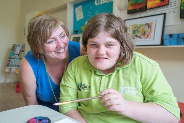 Girl smiling at camera with paintbrush and her teacher