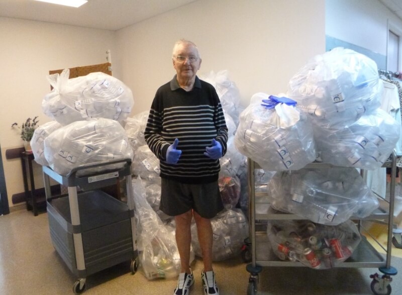 Man giving thumbs up surrounded by plastic bags filled with bottles