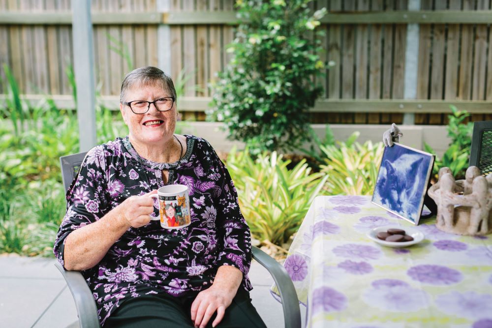 Lady sits in chair outside holding coffee cup and smiling