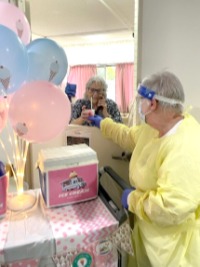 Worker in full PPE handing an icecream from an ice cream cart with balloons to an elderly woman