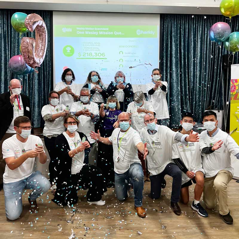 Group of people wearing white tshirts and masks celebrating with party poppers